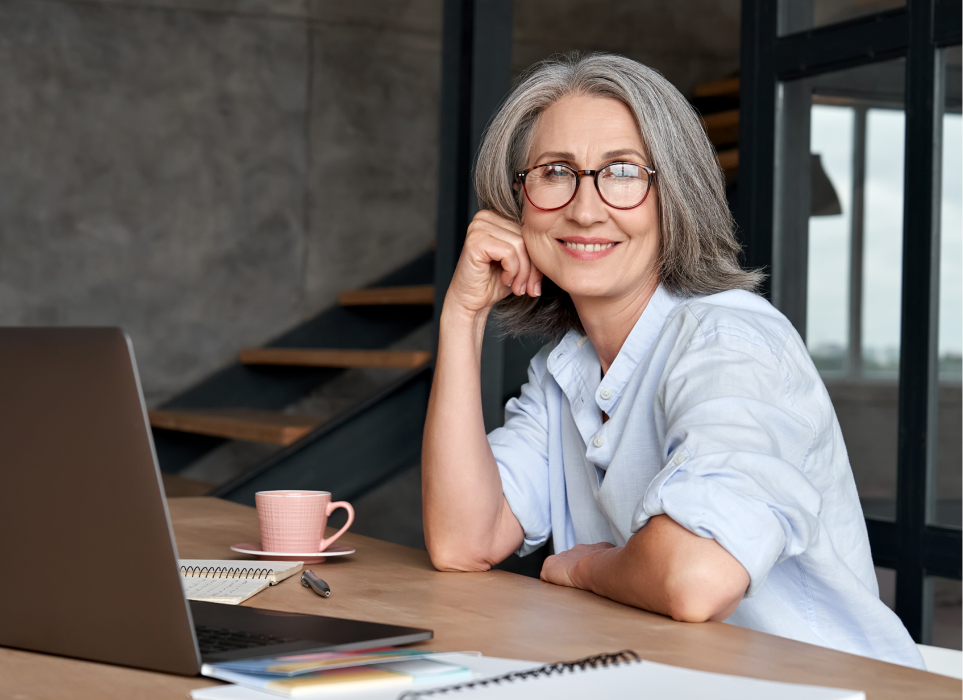 Middle Age Smiling Woman Siting at Desk With Laptop.jpeg Woman with white hair sitting at her computer smiling